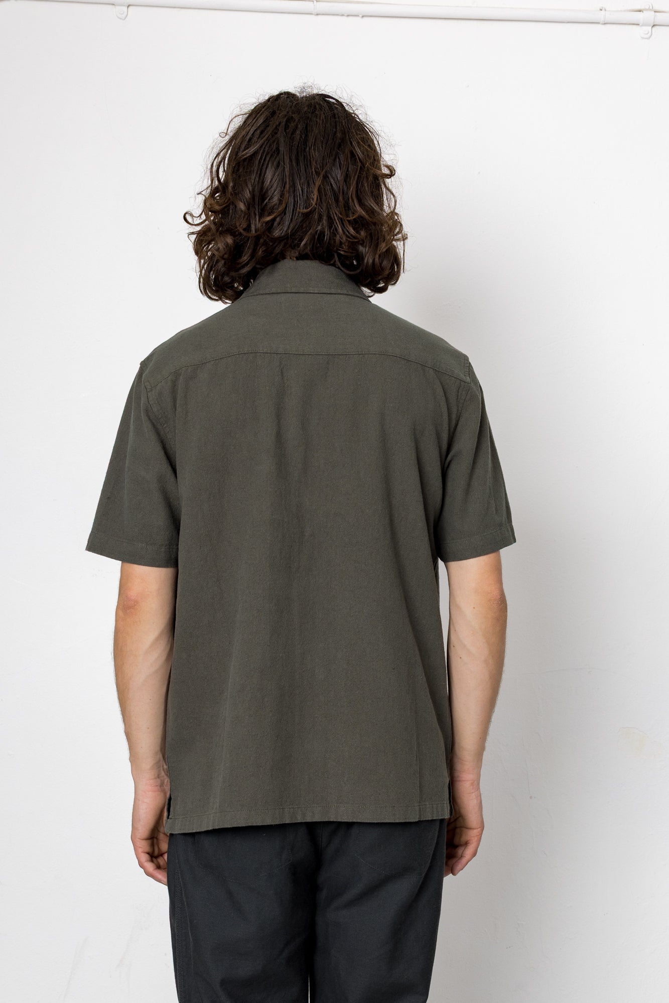 Person wearing a green shirt and black pants against a white background