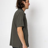 Man wearing a green shirt and dark pants against a white background
