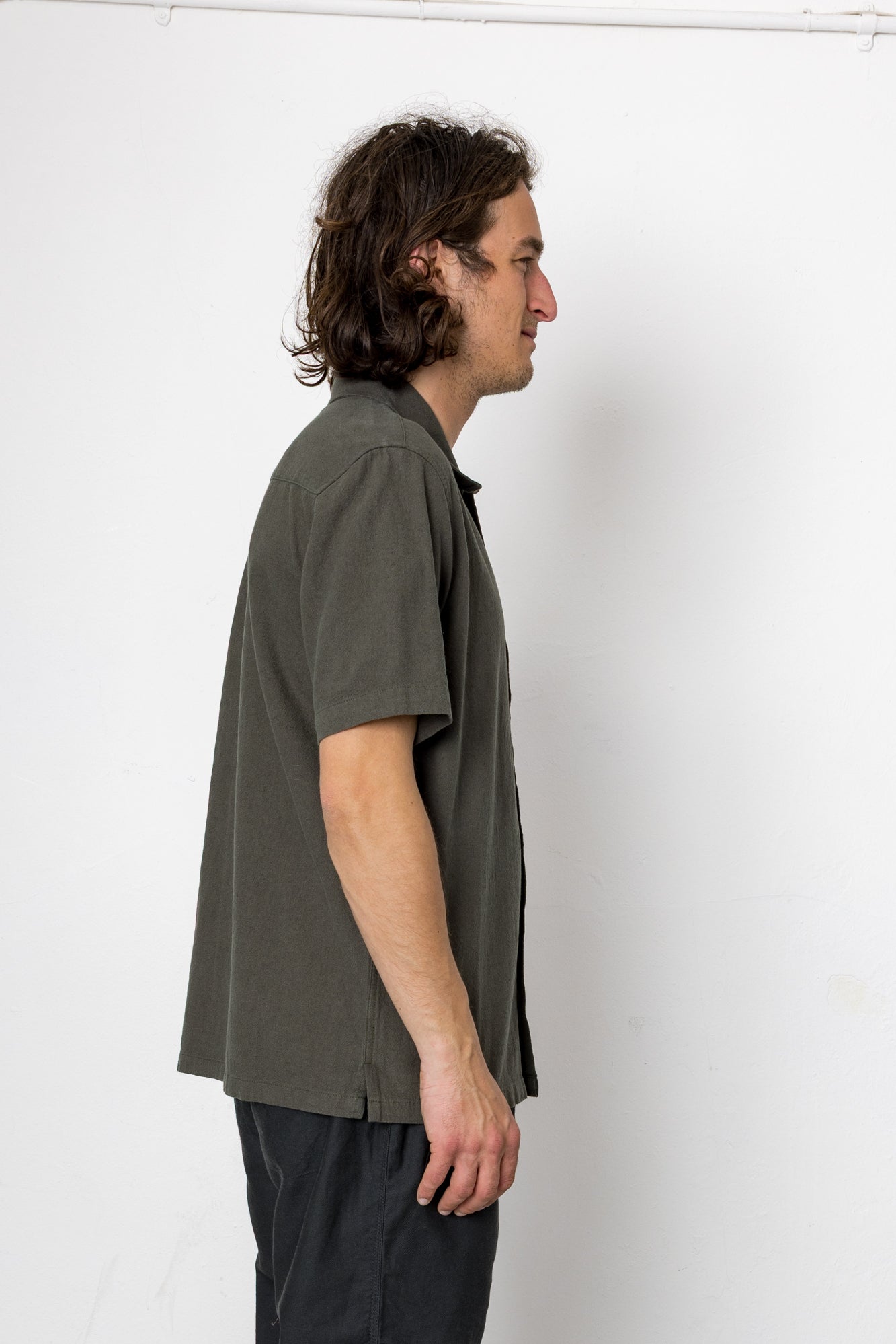 Man wearing a green shirt and dark pants against a white background