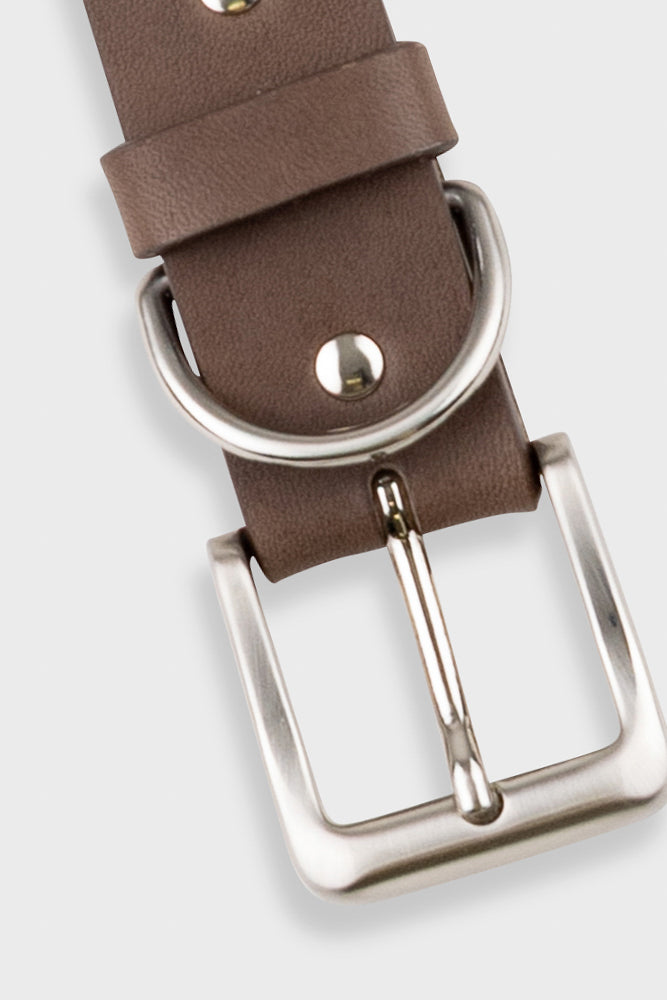 A close-up of a brown leather belt showing the silver-tone metal buckle, keeper loop, and rivets against a light gray background.