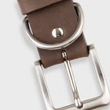 A close-up of a brown leather belt showing the silver-tone metal buckle, keeper loop, and rivets against a light gray background.