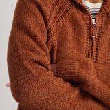 A close-up of a man wearing a chunky knit zip-up cardigan in a warm rust brown color, layered over a white and black striped t-shirt.