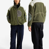 A man and a woman modeling an olive green fleece jacket with contrasting white shoulder panels, gray elbow patches, and a gray zippered chest pocket, shown from both front and back views against a plain white studio background.