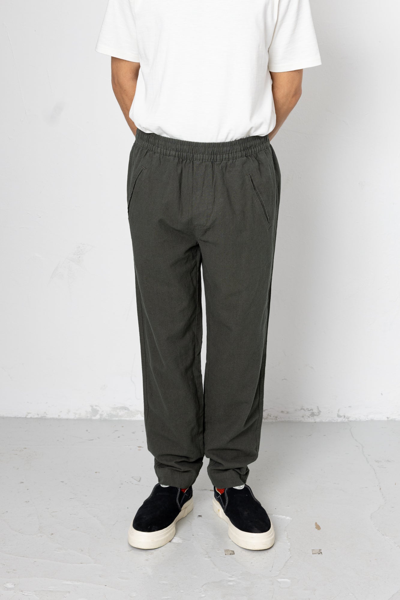 Person wearing dark gray pants and black shoes on a white background