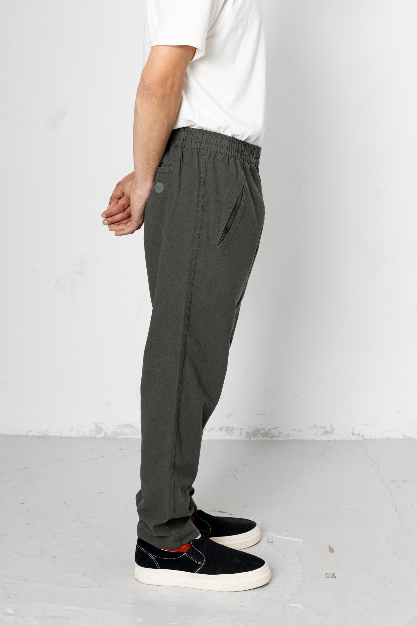 Person wearing dark gray pants and black sneakers on a white background