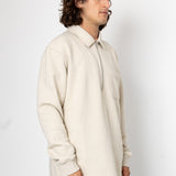 Man wearing a beige sweater and dark pants against a white background