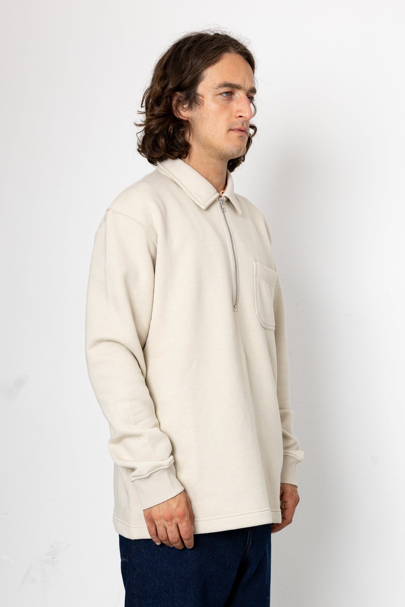 Man wearing a beige sweater and dark pants against a white background