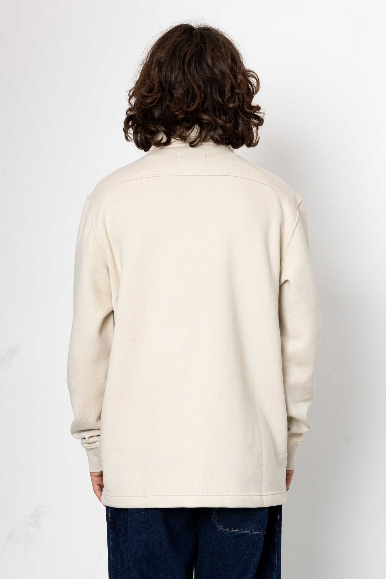 Person wearing a beige sweater with a plain white background