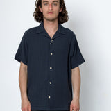 Man wearing a dark blue short-sleeve shirt with buttons against a white background