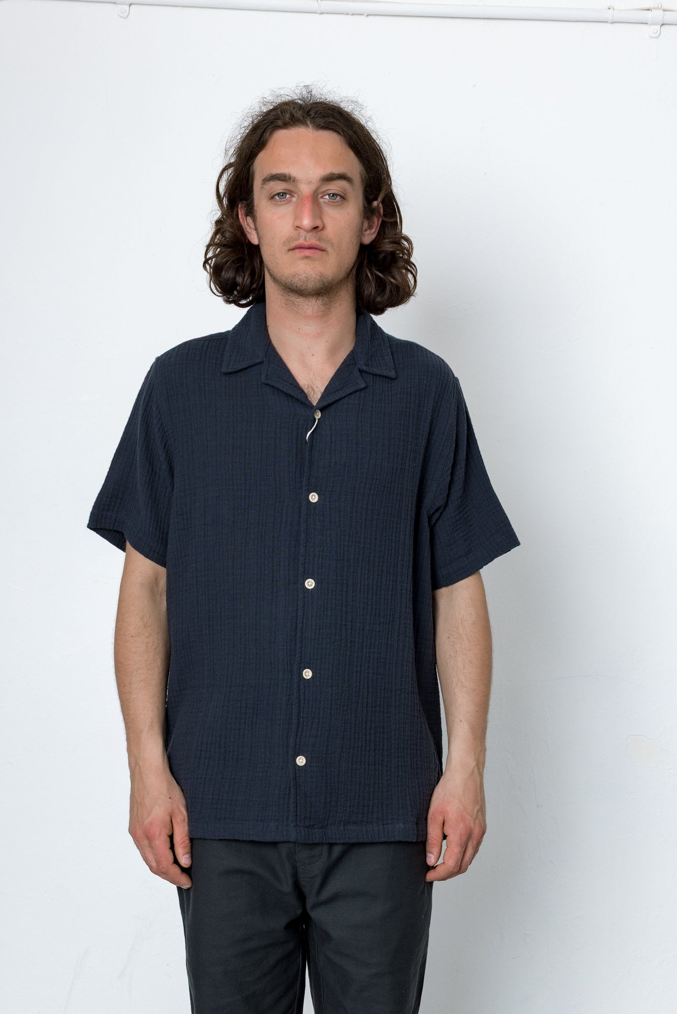 Man wearing a dark blue short-sleeve shirt with buttons against a white background