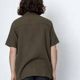 Person wearing a green shirt and dark pants against a white background