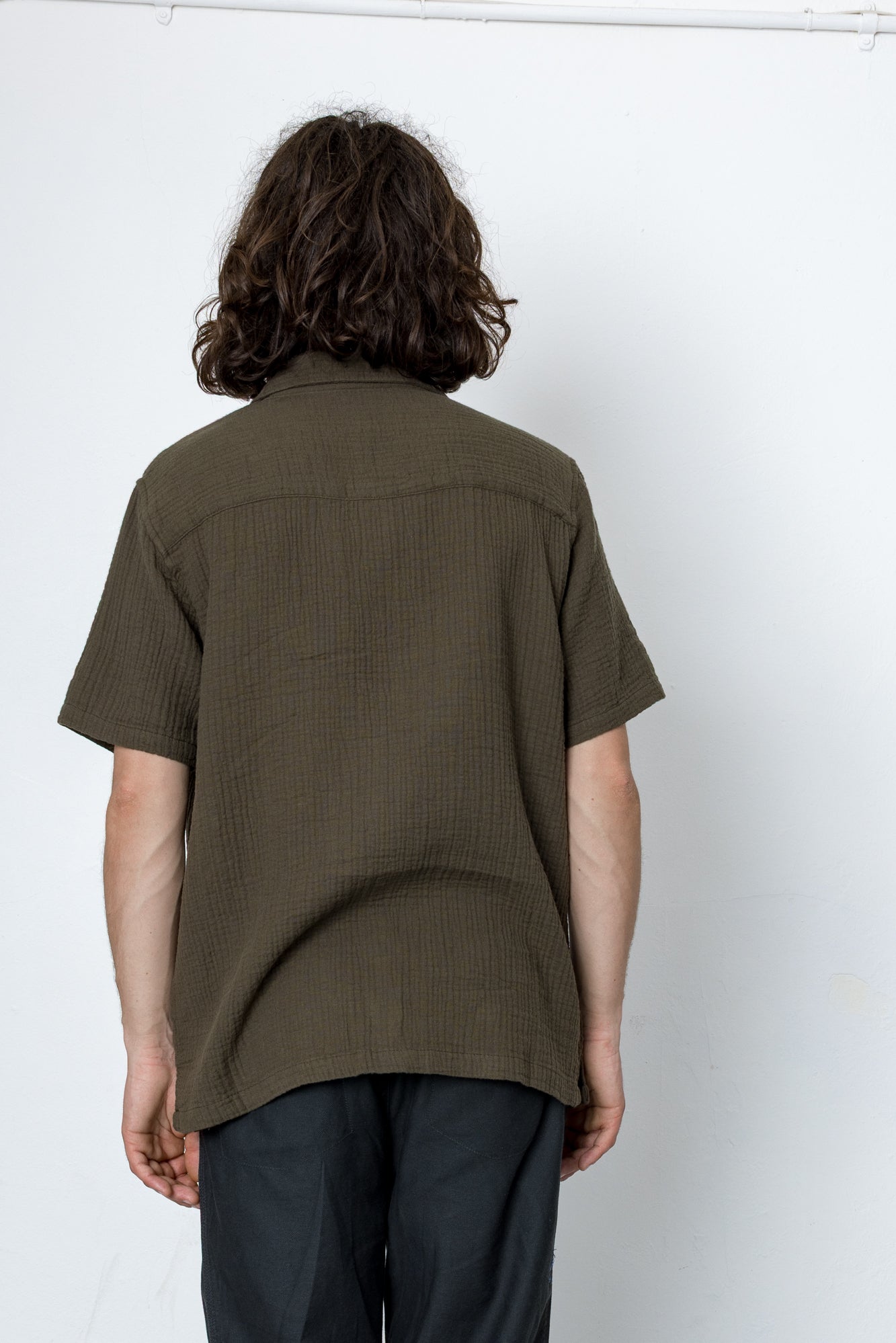 Person wearing a green shirt and dark pants against a white background