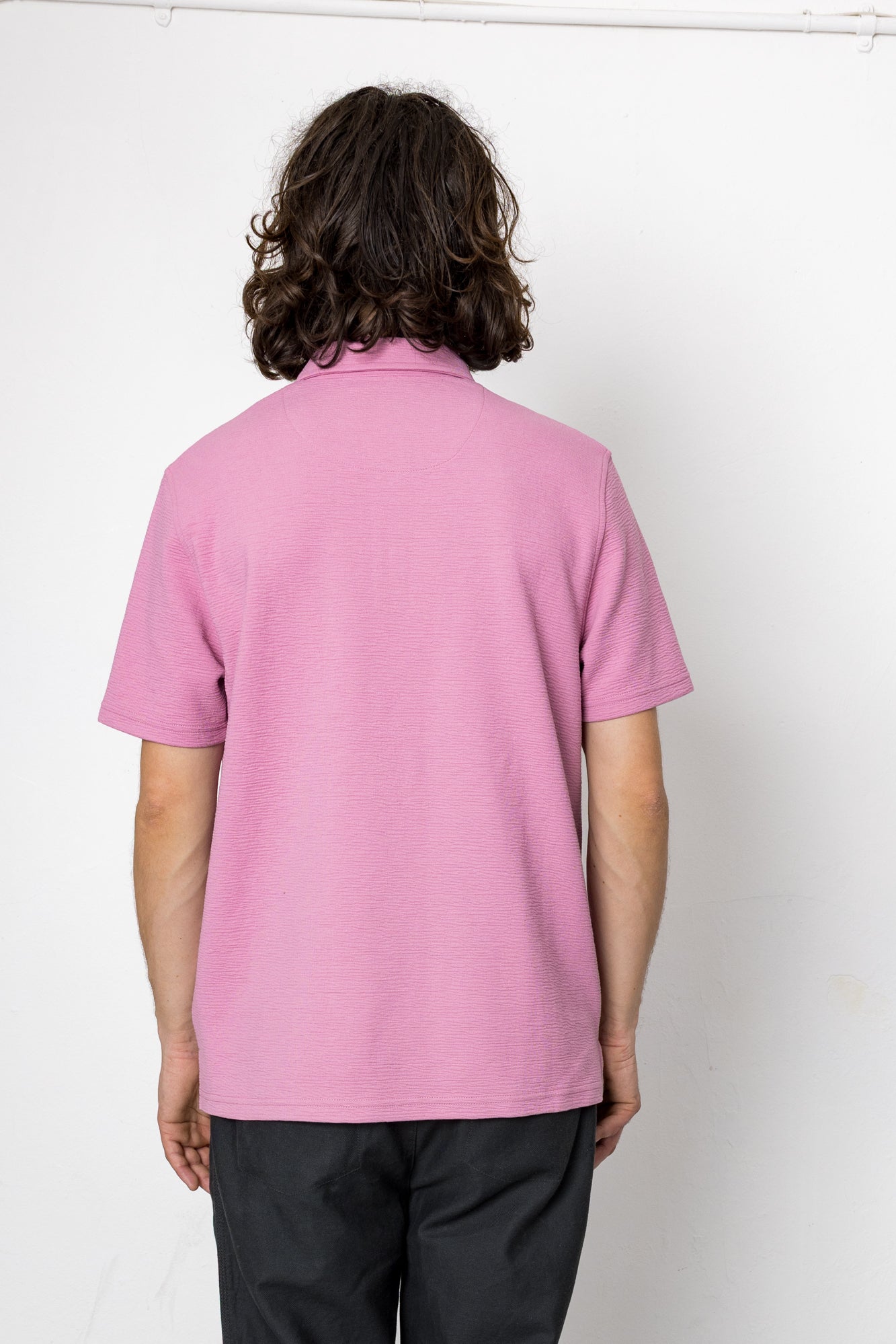 Person wearing a pink polo shirt against a white background