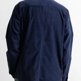 A man viewed from behind wearing a dark navy blue long-sleeve button-down shirt and green pants, against a plain white background.