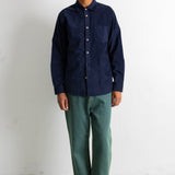 A man wearing a dark navy blue long-sleeve button-up shirt, green pants, and black-and-white sneakers, standing against a plain white wall.