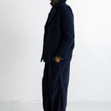 A model stands in profile wearing a dark navy blue textured jacket and matching wide-leg trousers, photographed against a plain white studio background.