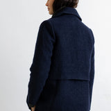 A woman shown from the back wearing a dark navy textured wool blazer and matching navy trousers against a plain white wall.