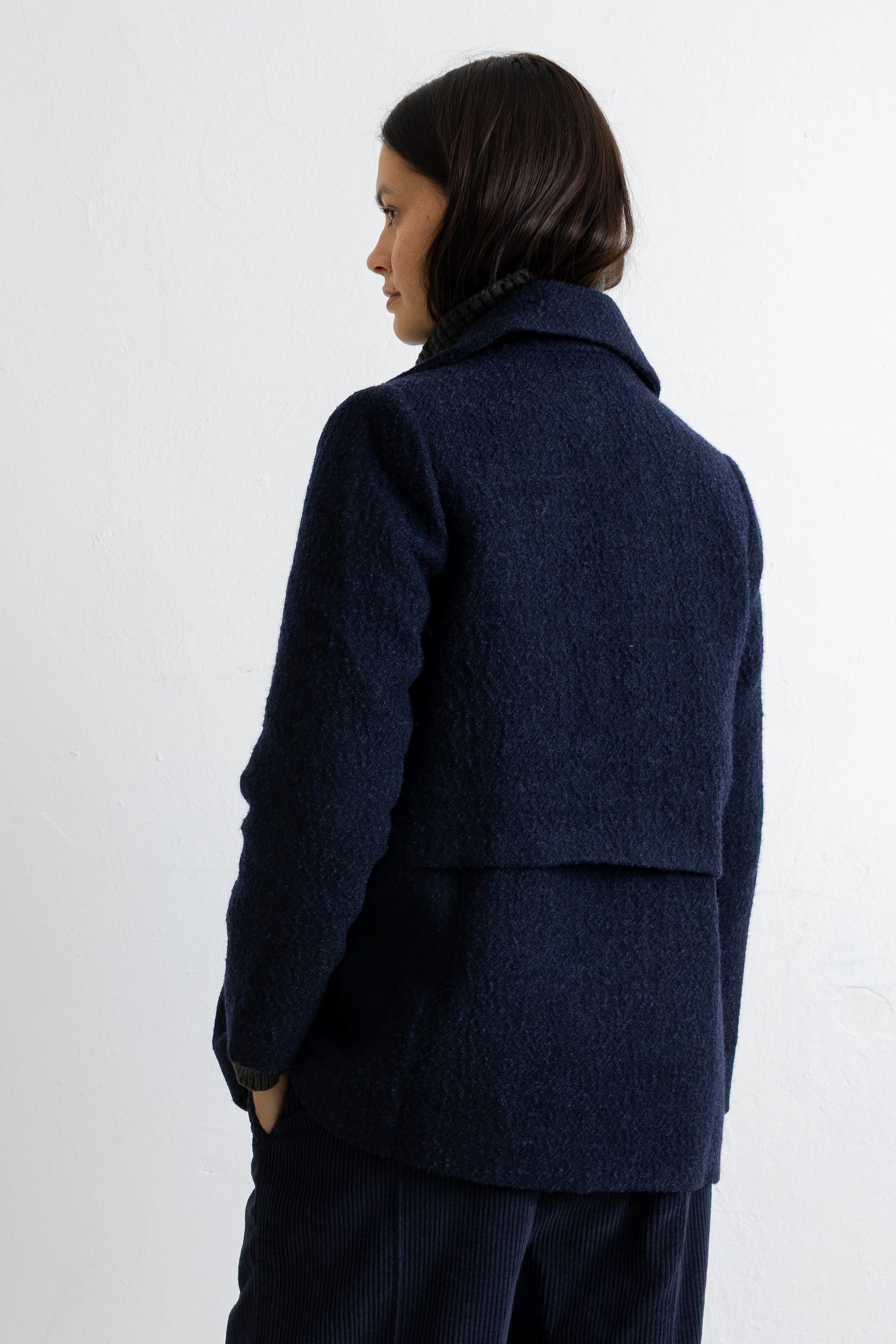 A woman shown from the back wearing a dark navy textured wool blazer and matching navy trousers against a plain white wall.