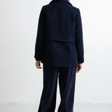 A model viewed from the back wearing a dark navy blue textured jacket and matching wide-leg trousers against a plain white studio background.