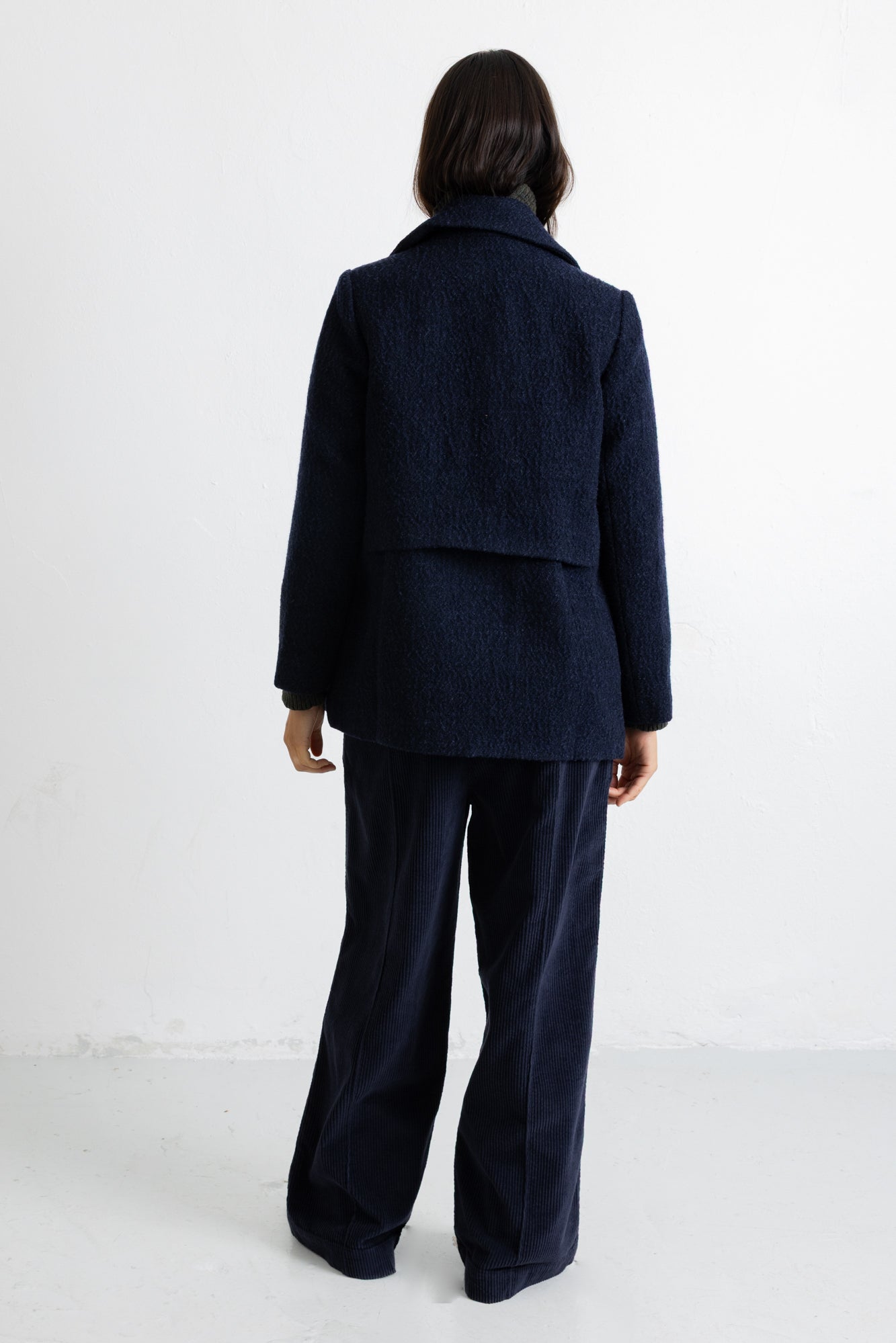 A model viewed from the back wearing a dark navy blue textured jacket and matching wide-leg trousers against a plain white studio background.