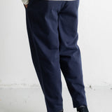 A person shown from the waist down wearing navy blue relaxed-fit trousers, a cream and navy striped long-sleeve shirt, and black high-top sneakers with white soles, standing against a white wall.