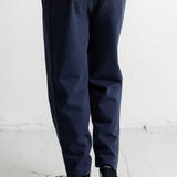 A person shown from the waist down wearing navy blue relaxed-fit pants, a cream and navy striped t-shirt, and black high-top sneakers with white soles, standing against a white textured wall.