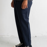 A person wearing dark navy blue relaxed-fit pants, a dark striped t-shirt, and black canvas high-top sneakers, standing against a white wall.