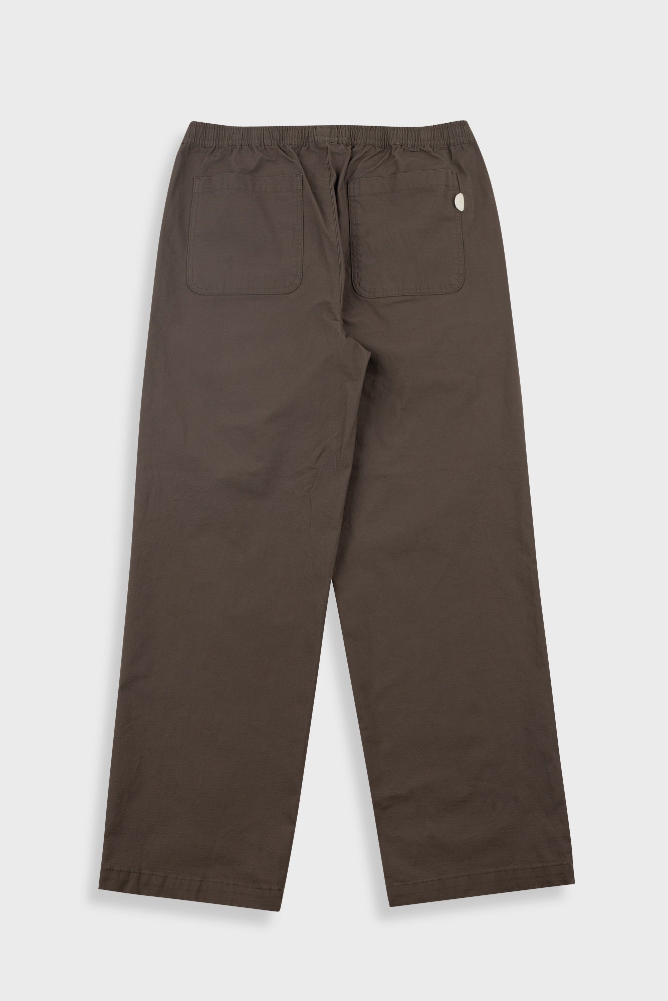 A pair of dark brown trousers shown from the back, featuring an elastic waistband, two large back patch pockets, and a small white circular logo on the upper right side, displayed against a light gray background.
