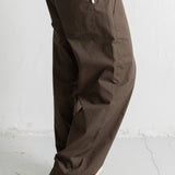 A person wearing loose, wide-leg brown pants with a white t-shirt and navy low-top sneakers, shown from the waist down against a light gray wall and floor.