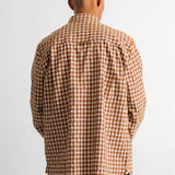 A man viewed from behind wearing a brown and white gingham check long-sleeve shirt and dark jeans against a plain white background.