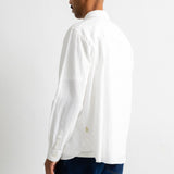 A man shown from the back wearing a white long-sleeve linen shirt and dark blue jeans, standing against a plain white studio background.