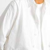 Close-up of a person wearing a white long-sleeve button-up shirt over a white undershirt, against a plain light background.