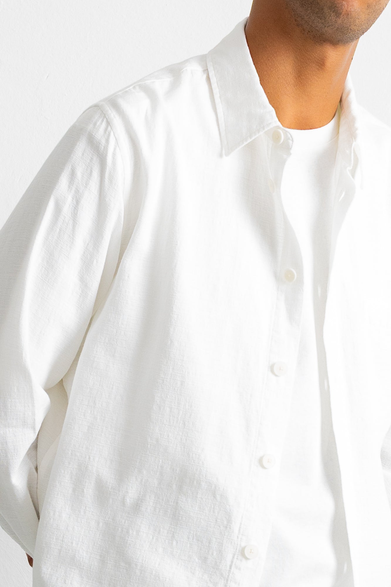 Close-up of a person wearing a white long-sleeve button-up shirt over a white undershirt, against a plain light background.