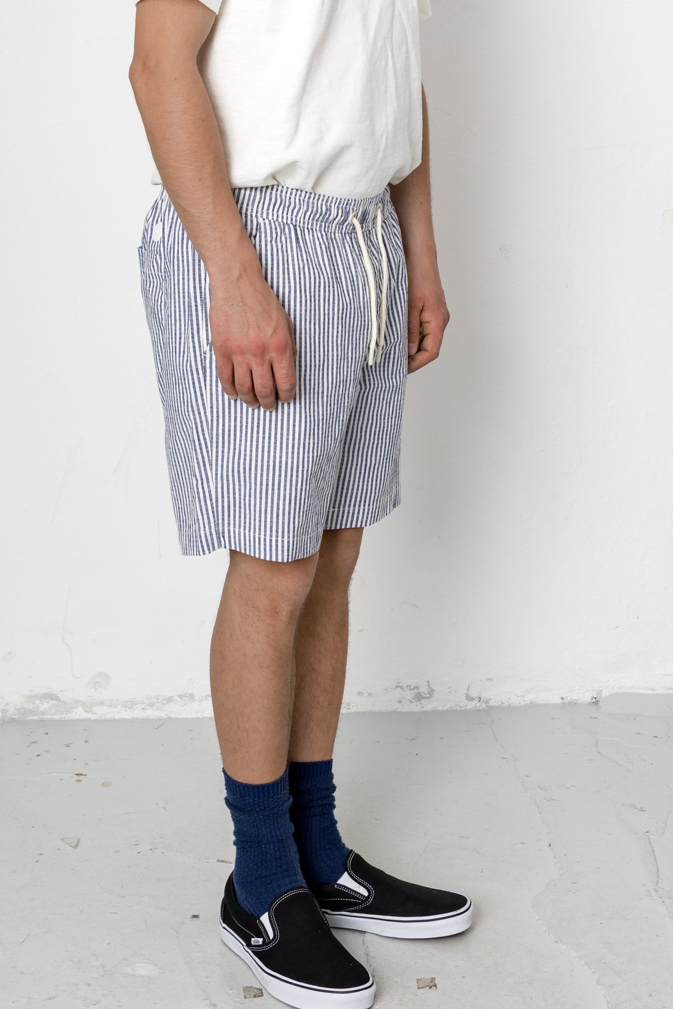Person wearing blue and white striped shorts with a white shirt and black shoes on a plain background