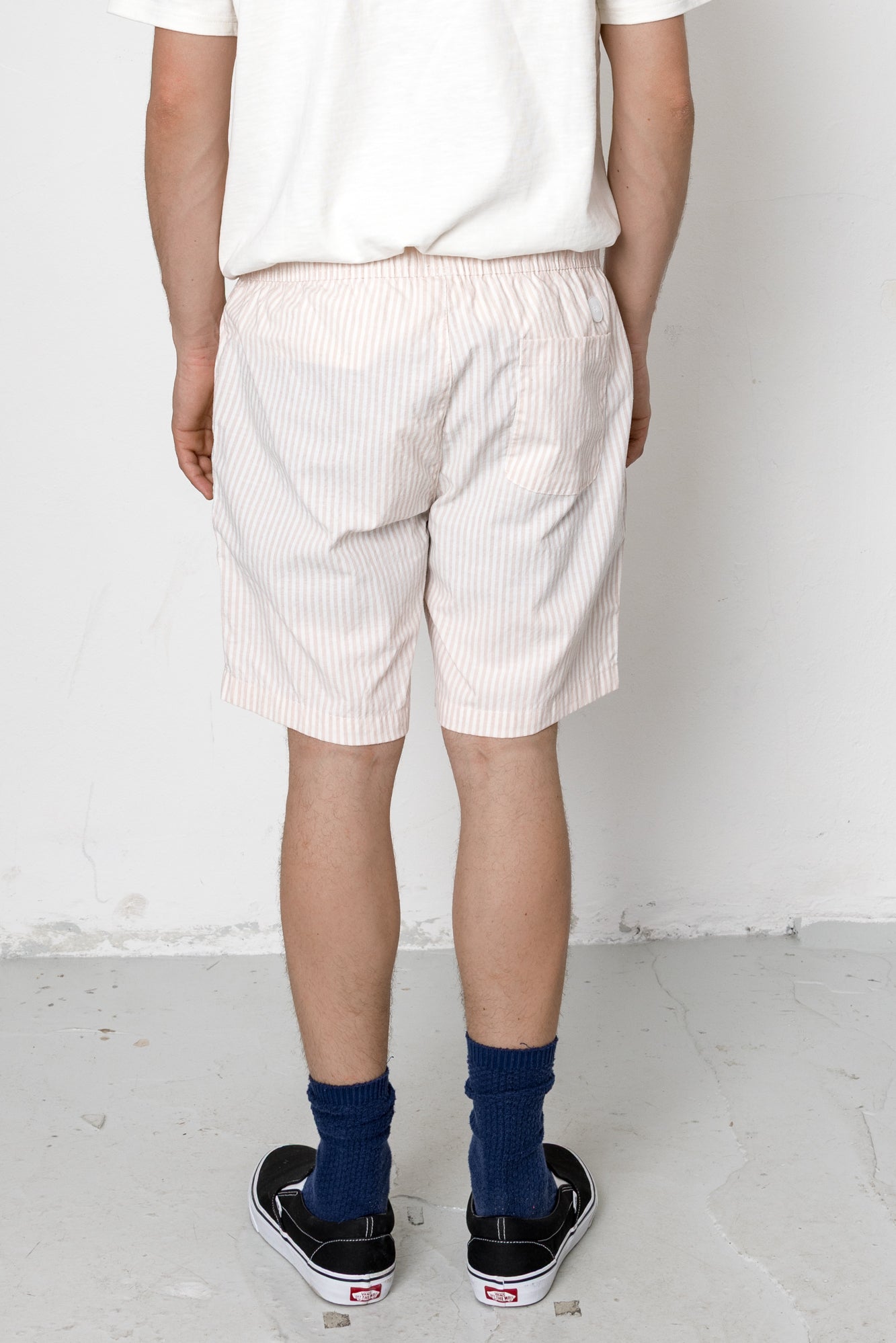 Person wearing white striped shorts and black sneakers on a plain background
