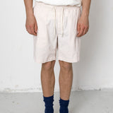 Person wearing white shorts with a subtle pattern, a white shirt, blue socks, and black shoes on a plain background.