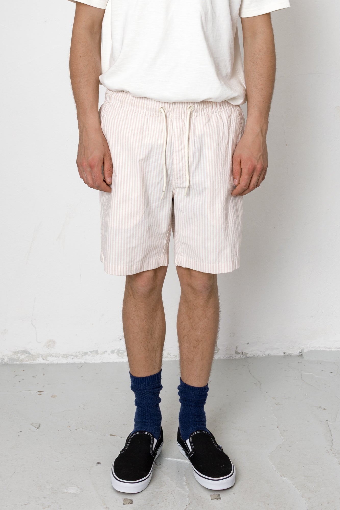 Person wearing white shorts with a subtle pattern, a white shirt, blue socks, and black shoes on a plain background.