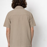 Person wearing a beige short-sleeve shirt against a white background