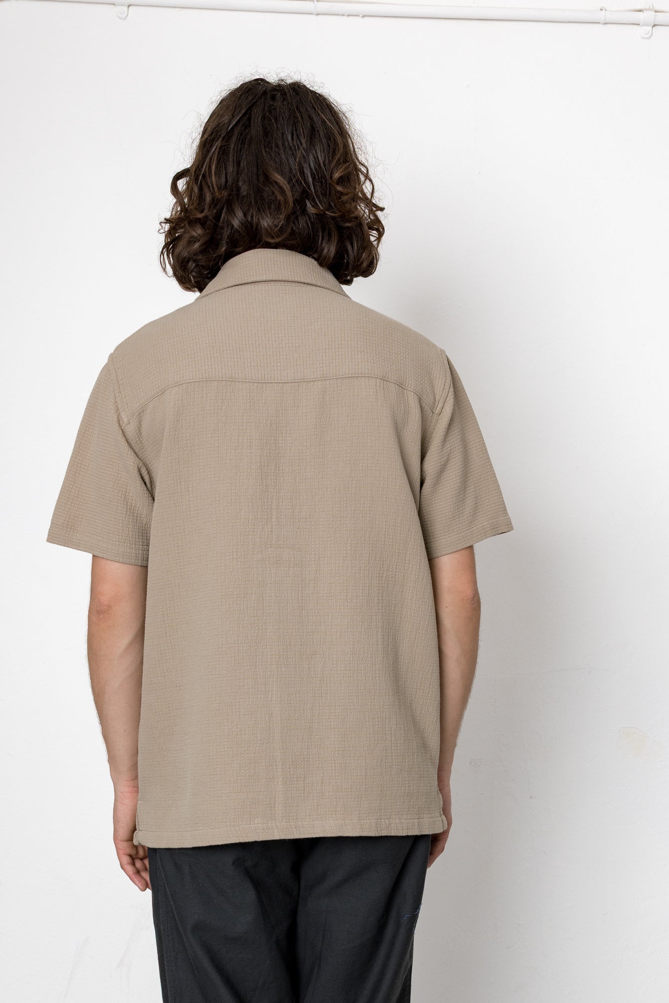 Person wearing a beige short-sleeve shirt against a white background