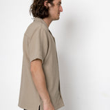 Man wearing a beige short-sleeve shirt against a white background