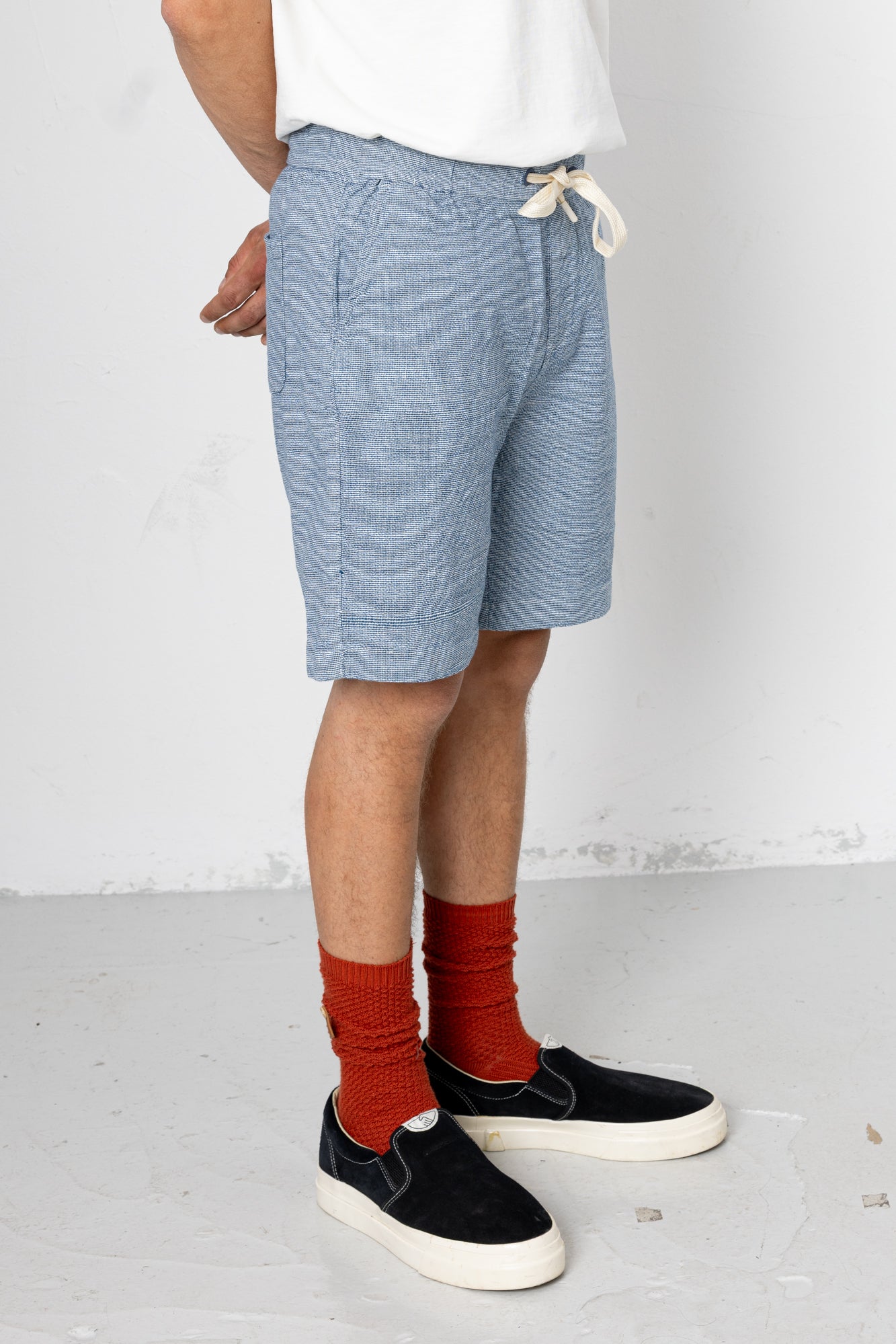 Person wearing blue shorts, black sneakers, and red socks on a white background