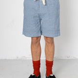 Person wearing blue shorts, white shirt, red socks, and black sneakers on a plain background