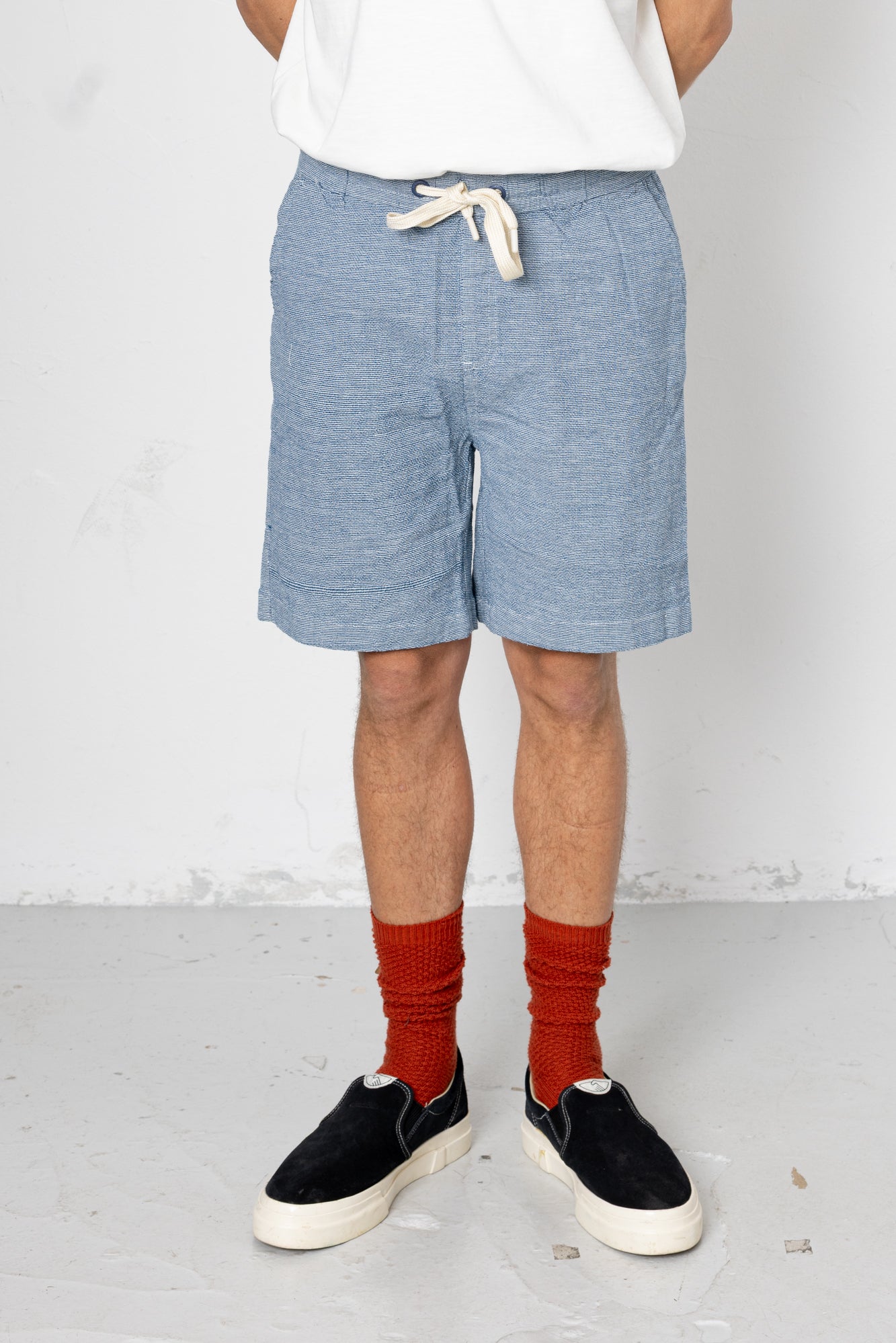 Person wearing blue shorts, white shirt, red socks, and black sneakers on a plain background