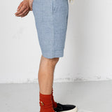 Person wearing light blue shorts, black sneakers, and red socks on a white background