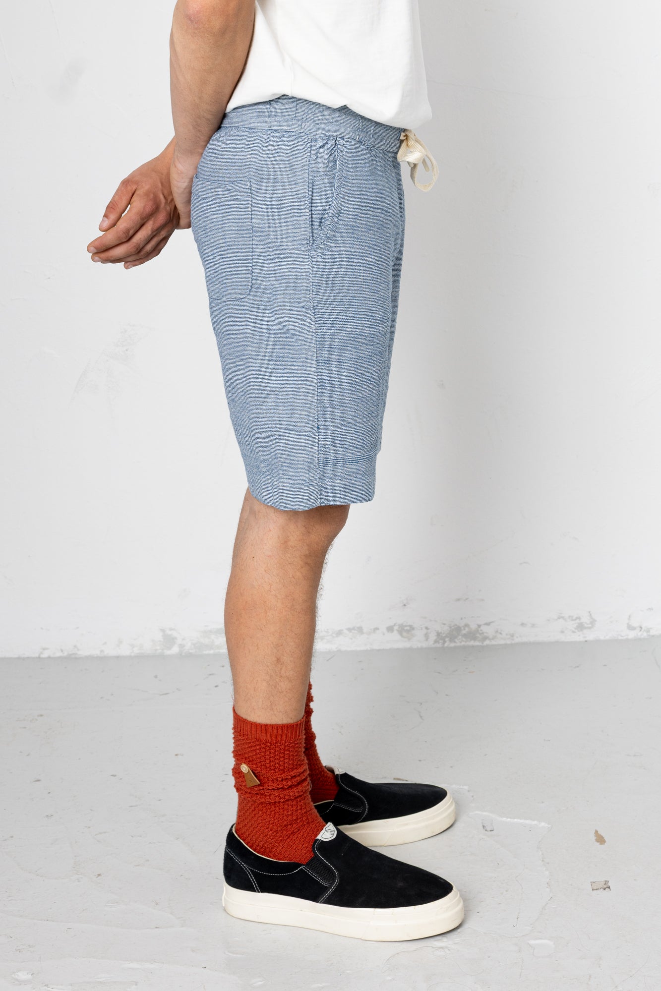 Person wearing light blue shorts, black sneakers, and red socks on a white background