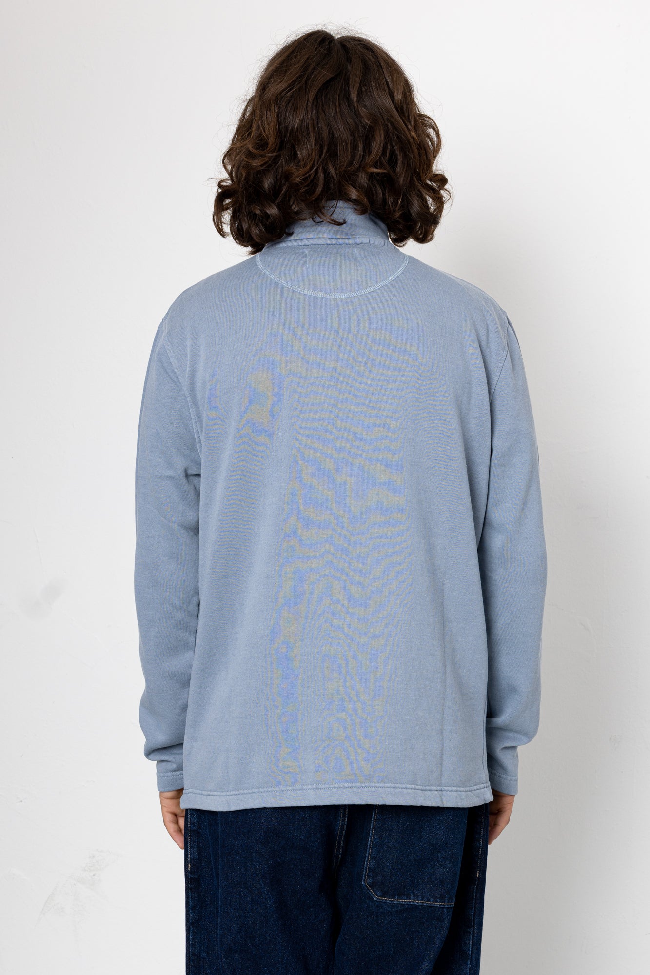 Person wearing a light blue long-sleeve shirt with a pattern on the back against a white background