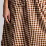 A close-up of a brown and beige gingham checkered skirt with a white ribbed top visible at the waist, worn by a model.
