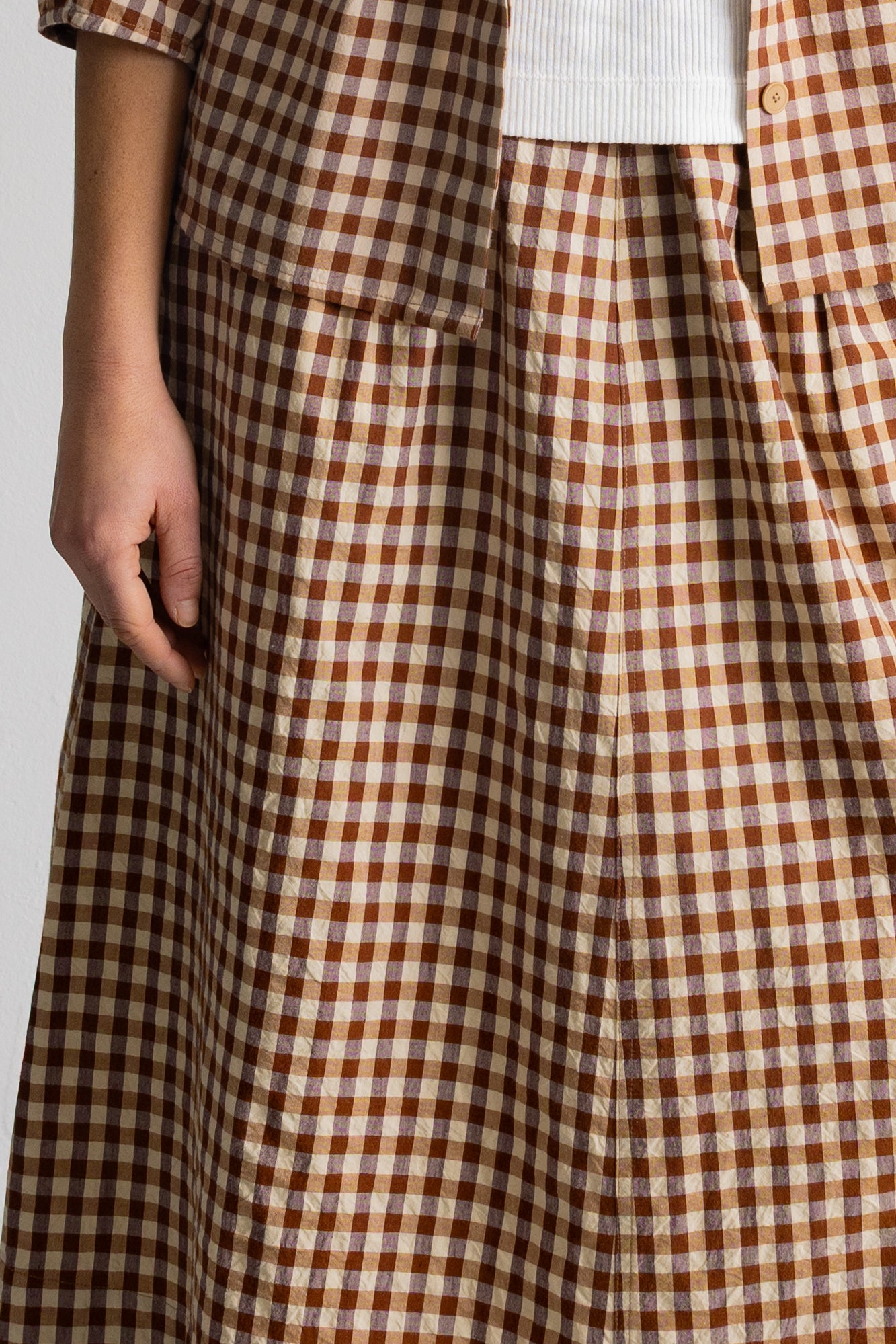 A close-up of a brown and beige gingham checkered skirt with a white ribbed top visible at the waist, worn by a model.