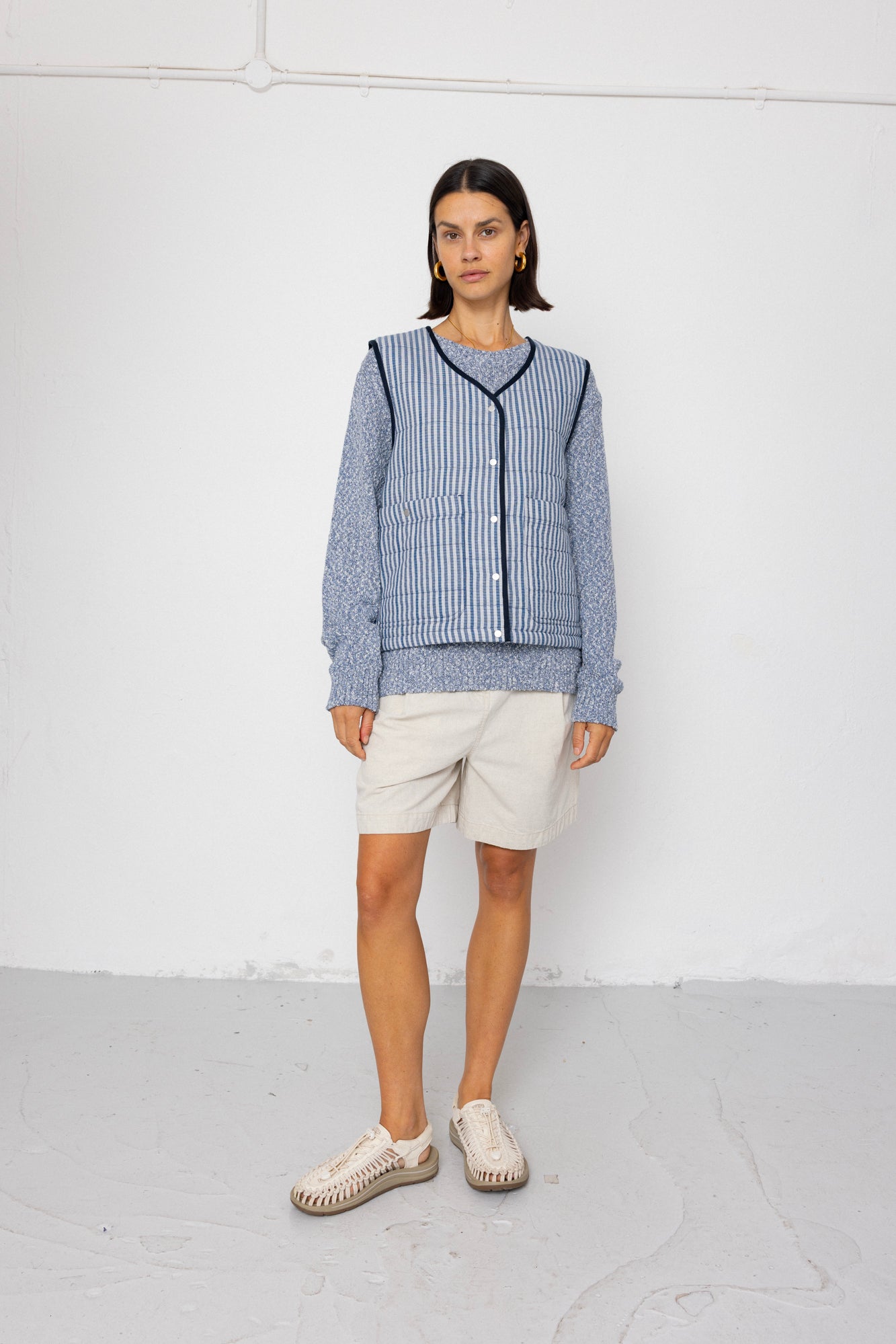 Woman wearing a blue striped vest and white shorts against a white background