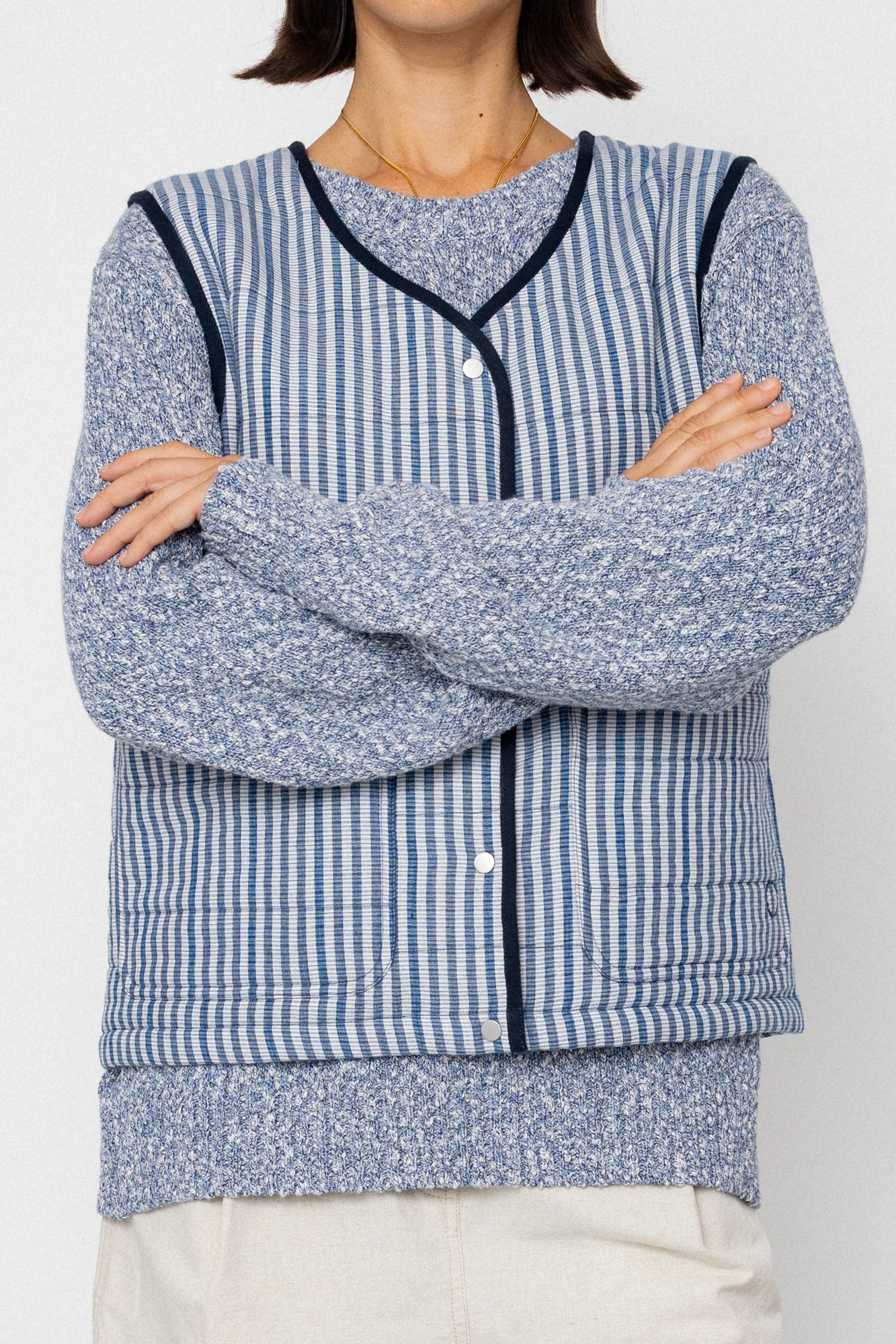 Person wearing a blue and white striped vest over a jumper with a plain background
